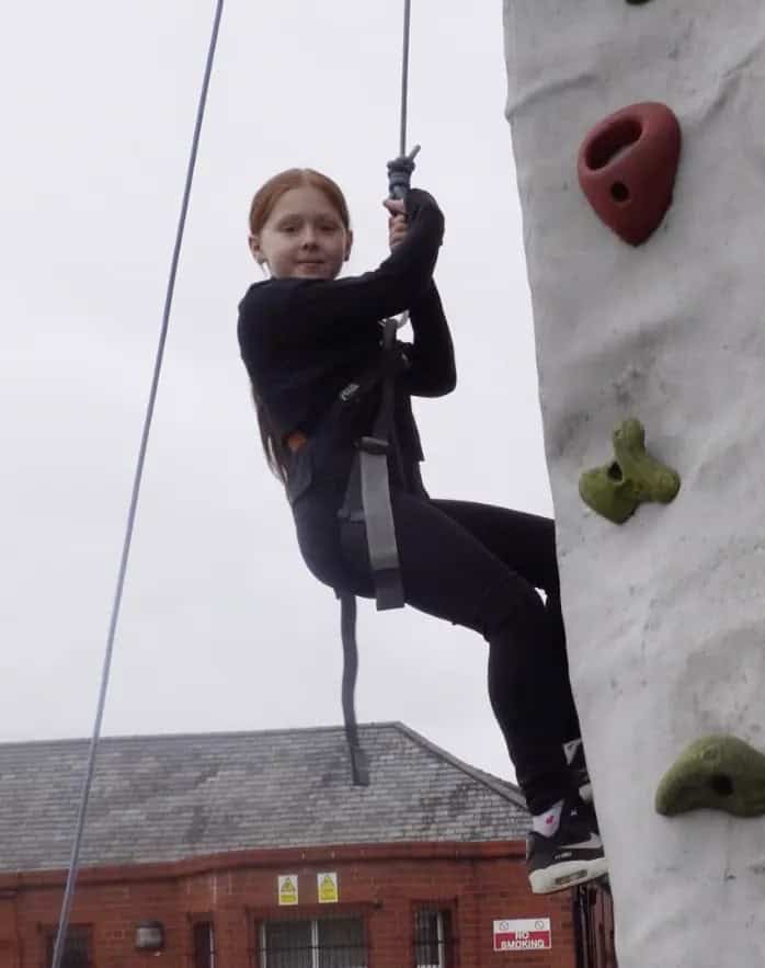 Pupil rock climbing and smiling at camera